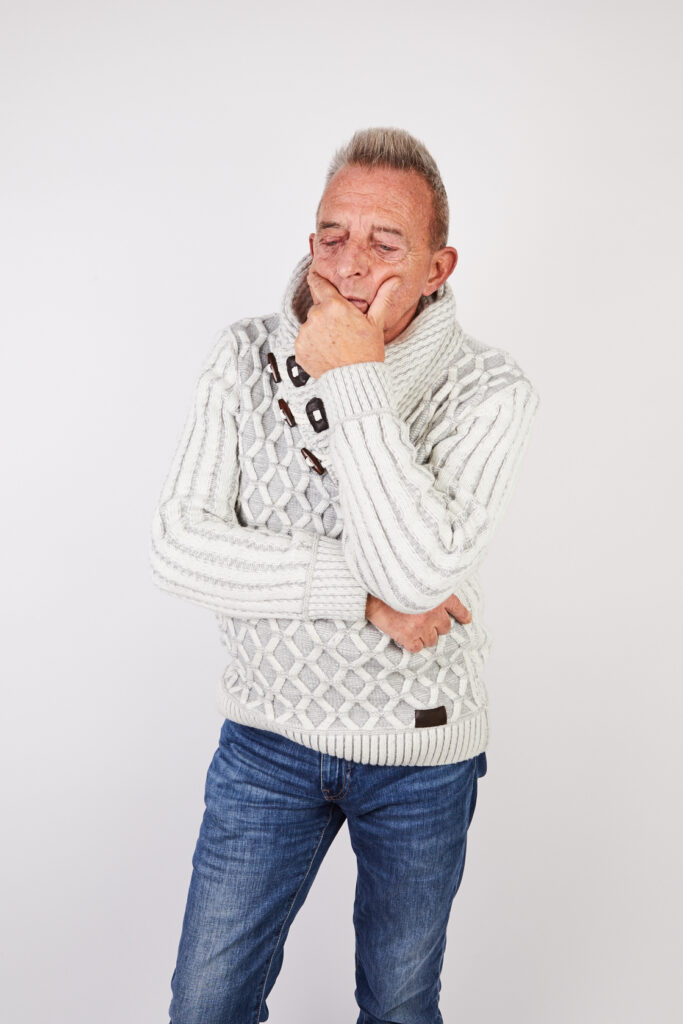 Older man in white jumper standing thoughtfully with his hand in face. Portrait.