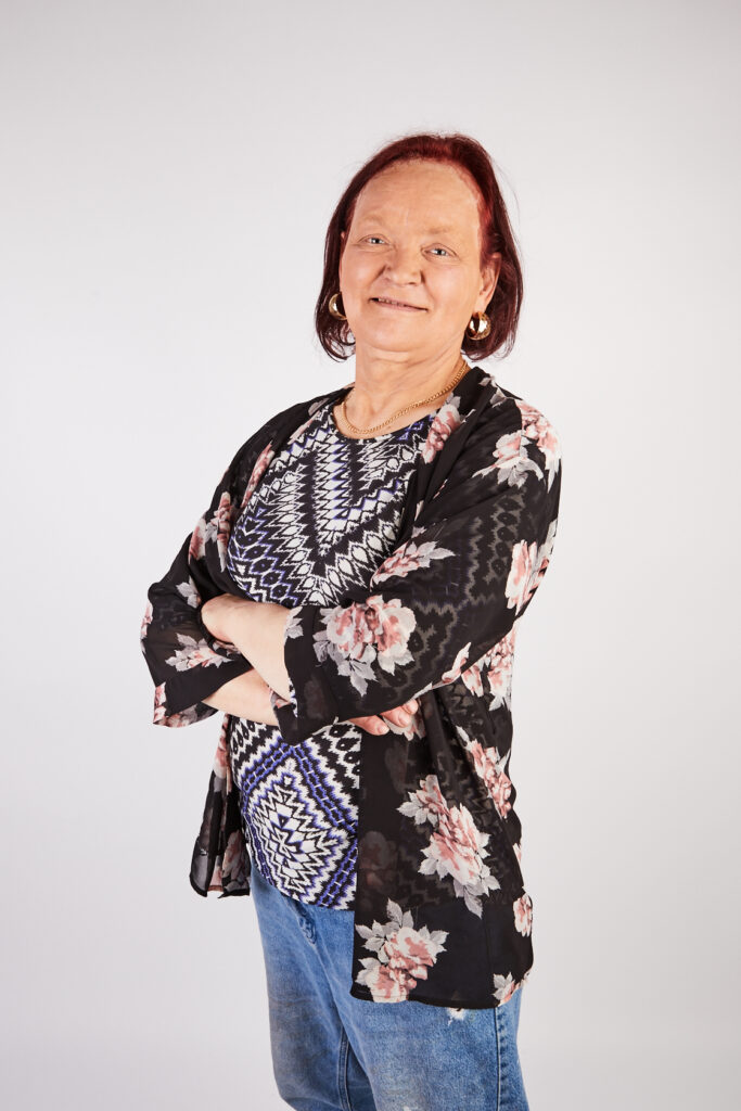Older woman with short red hair in floral blazer standing confidently with her arms crossed in front of white background. Portrait.