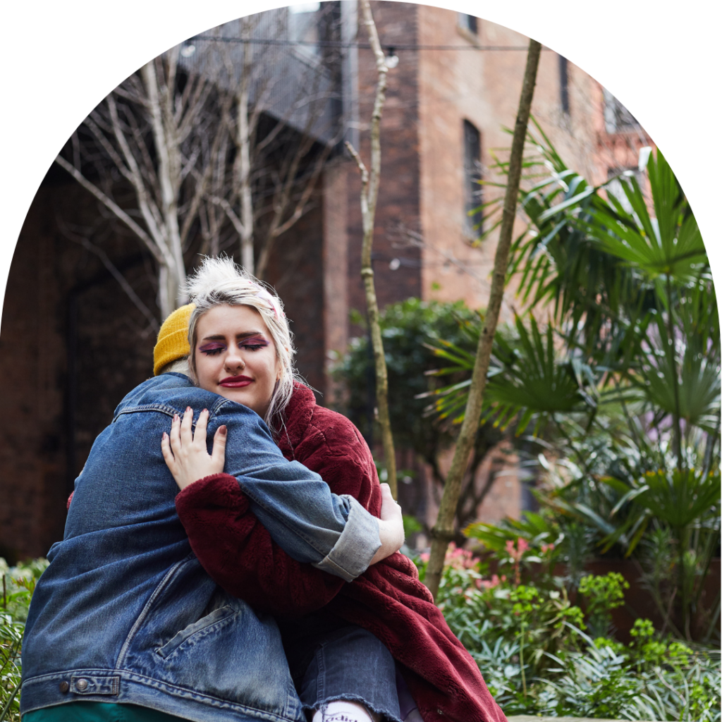 A fem-presenting and a masc-presenting people hugging each other friendly in garden.