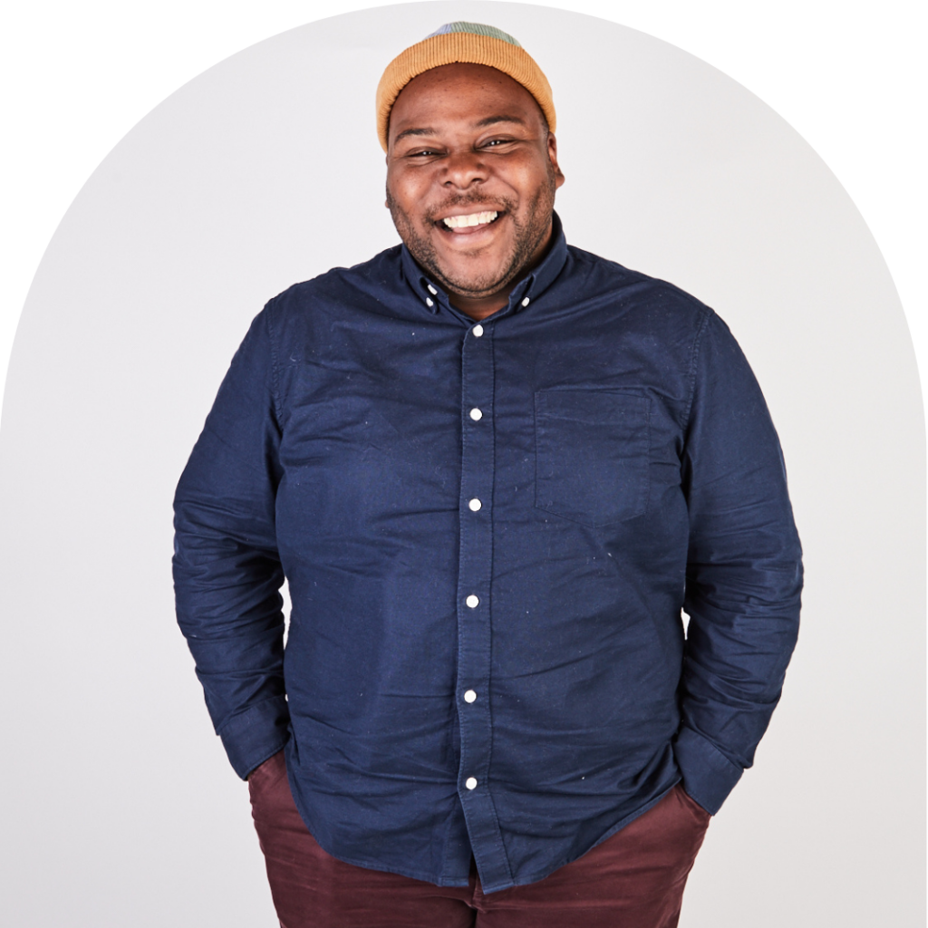 A black masc-presenting person smiling at the camera. Portrait.