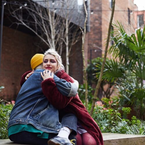 A fem-presenting and a masc-presenting people hugging each other friendly in garden.