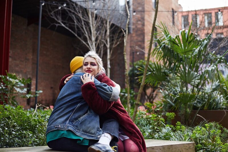 A fem-presenting and a masc-presenting people hugging each other friendly in garden.