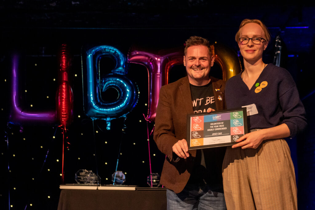 On stage, volunteer award winner and presenter holing the award together, smiling at camera.
