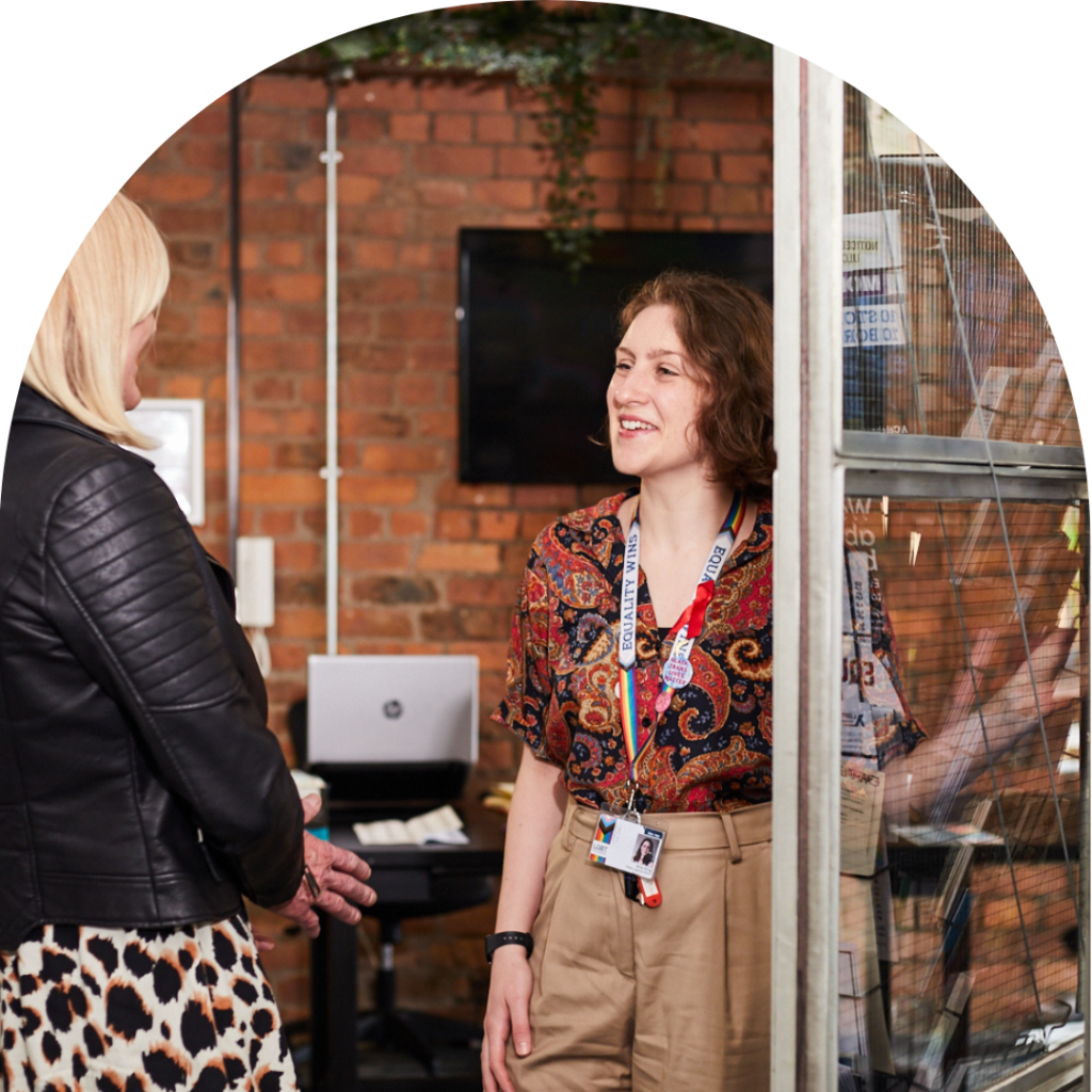 LGBT Foundation employee opening the door, smiling and inviting a visitor with blonde hair in.