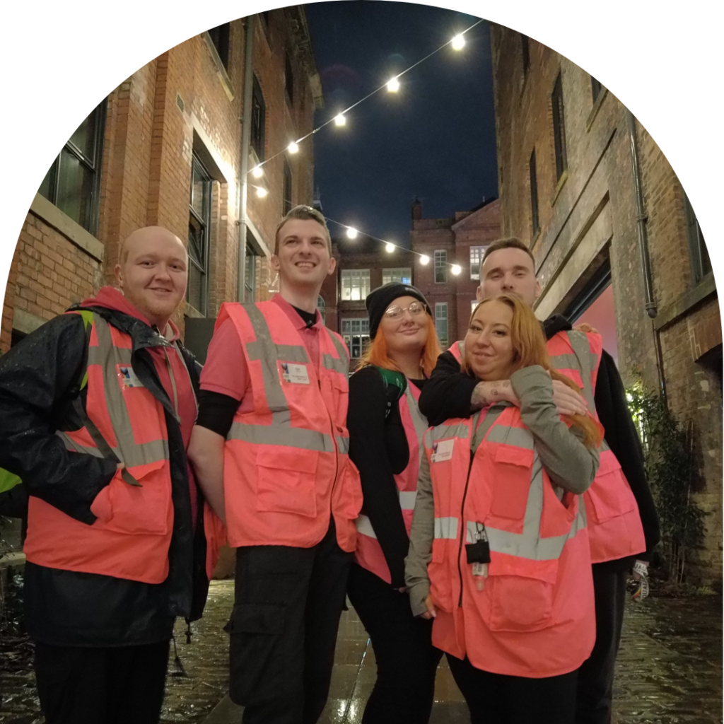 A group of village angels stand together smiling in the dark Manchester village street